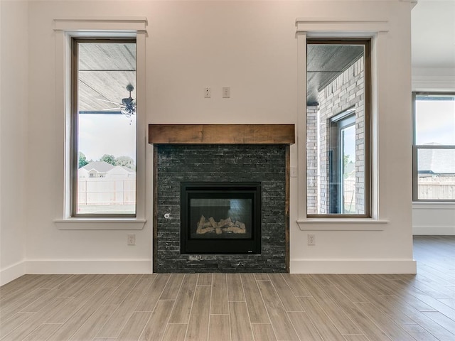 unfurnished living room featuring a stone fireplace, baseboards, and wood tiled floor