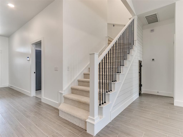 stairway featuring wood finish floors, visible vents, baseboards, and a high ceiling