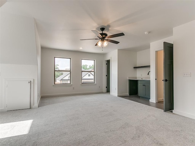 unfurnished living room with a sink, baseboards, a ceiling fan, and carpet floors