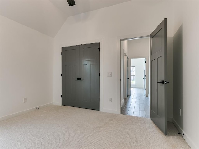 unfurnished bedroom featuring a closet, light colored carpet, baseboards, and vaulted ceiling