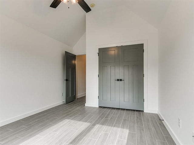 unfurnished bedroom with high vaulted ceiling, a closet, baseboards, ceiling fan, and wood tiled floor