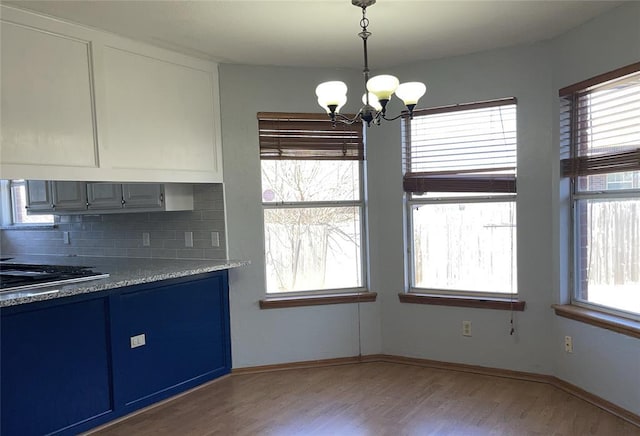 kitchen featuring backsplash, blue cabinetry, wood finished floors, hanging light fixtures, and a notable chandelier