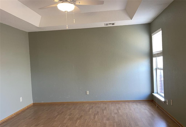 empty room featuring a tray ceiling, visible vents, light wood finished floors, and ceiling fan