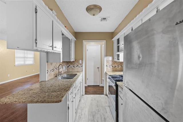 kitchen with light wood-style flooring, a sink, stainless steel appliances, white cabinets, and decorative backsplash