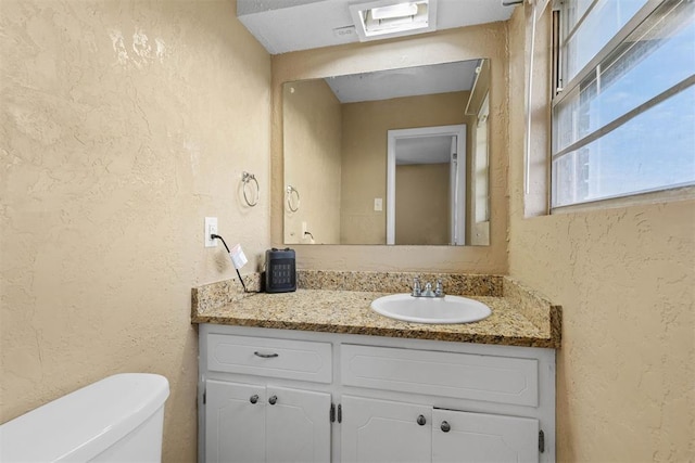 bathroom with toilet, vanity, and a textured wall