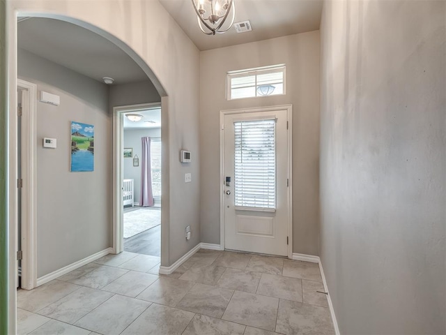 entrance foyer featuring an inviting chandelier, visible vents, baseboards, and arched walkways