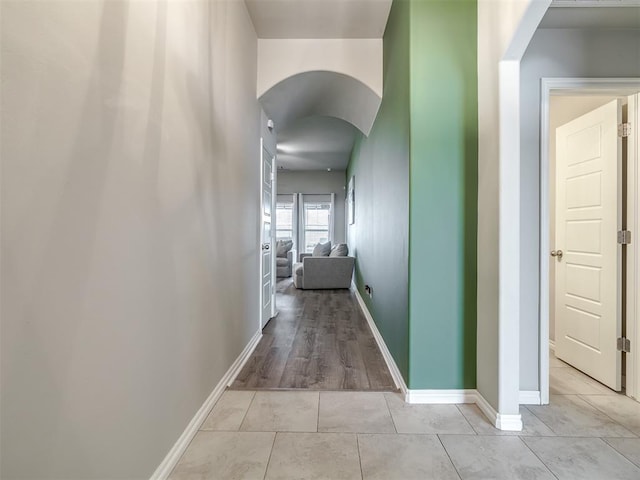 hall featuring light tile patterned floors, baseboards, and arched walkways