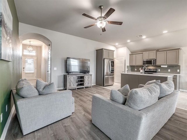 living area with light wood-style flooring, baseboards, arched walkways, and ceiling fan