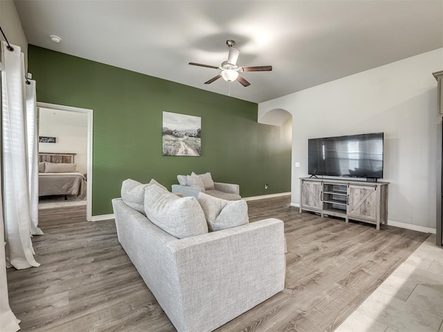 living area with baseboards, arched walkways, wood finished floors, and a ceiling fan