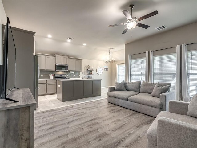 living room featuring light wood-style floors, vaulted ceiling, ceiling fan with notable chandelier, and visible vents