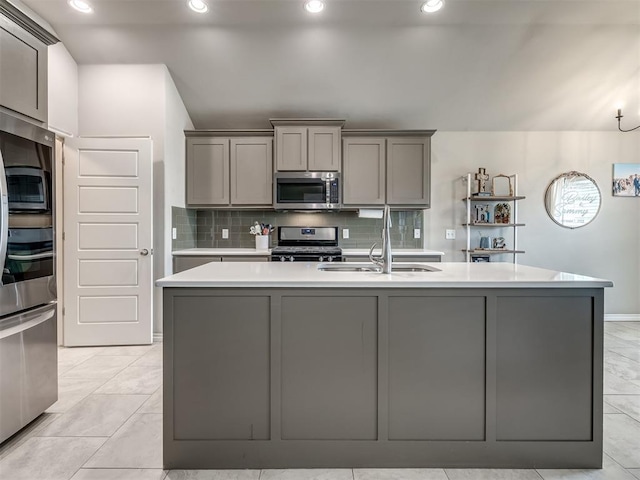 kitchen with backsplash, gray cabinetry, light countertops, stainless steel appliances, and a kitchen island with sink