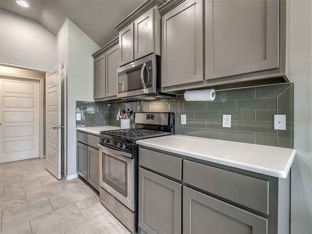 kitchen with tasteful backsplash, light countertops, vaulted ceiling, gray cabinets, and appliances with stainless steel finishes