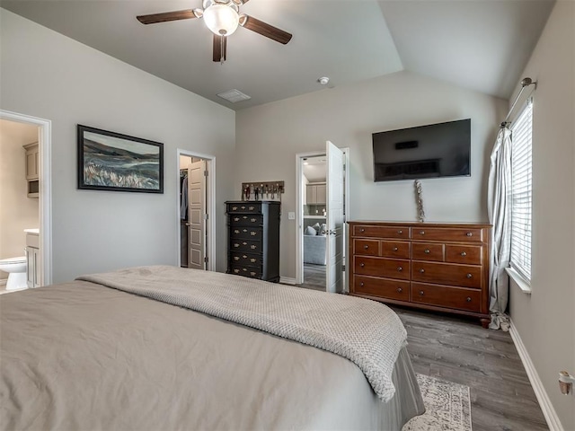 bedroom with connected bathroom, a walk in closet, baseboards, vaulted ceiling, and wood finished floors