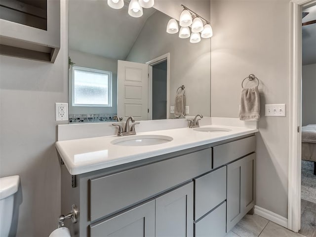 ensuite bathroom featuring double vanity, toilet, lofted ceiling, and a sink