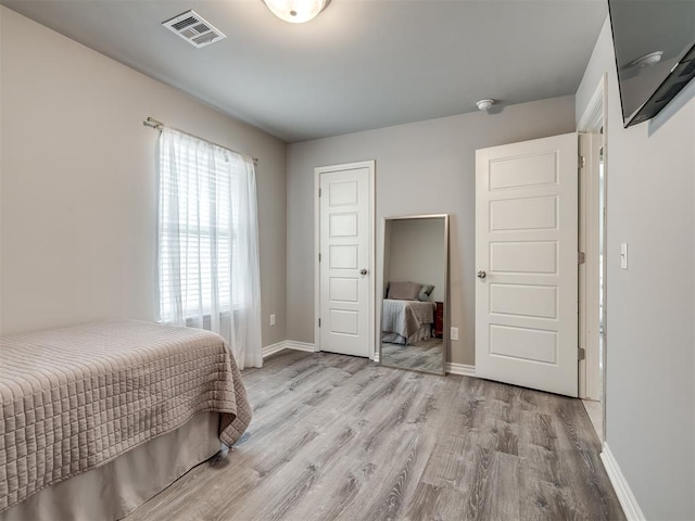 bedroom with wood finished floors, visible vents, a closet, and baseboards