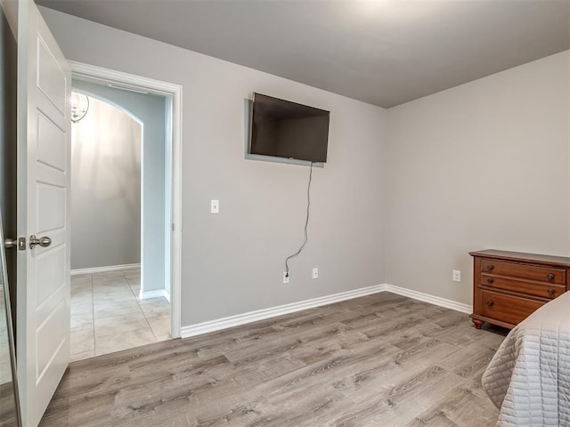 bedroom featuring arched walkways, light wood-style flooring, and baseboards