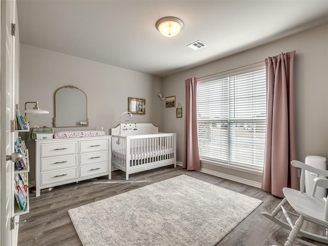 bedroom with visible vents, a crib, and dark wood-style flooring