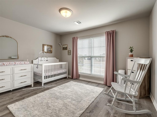 bedroom featuring visible vents, baseboards, a nursery area, and dark wood finished floors