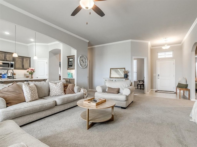 living room featuring baseboards, ceiling fan, ornamental molding, light carpet, and arched walkways