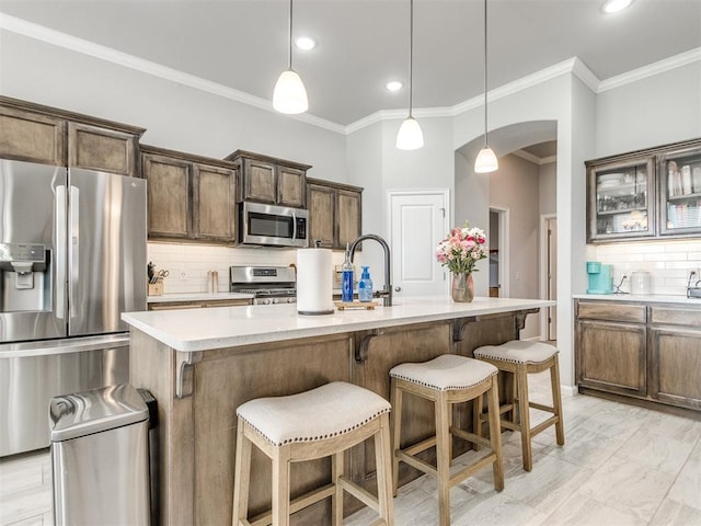 kitchen with arched walkways, decorative backsplash, light countertops, appliances with stainless steel finishes, and a kitchen bar