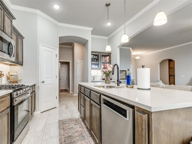 kitchen featuring a kitchen island with sink, a sink, stainless steel appliances, arched walkways, and crown molding