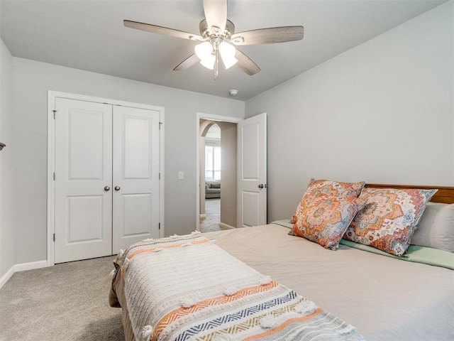 carpeted bedroom featuring baseboards, a ceiling fan, a closet, and arched walkways