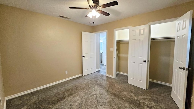 unfurnished bedroom with a ceiling fan, baseboards, visible vents, dark colored carpet, and two closets