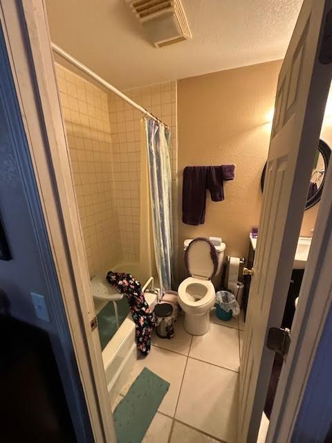 bathroom featuring visible vents, shower / bath combo, tile patterned flooring, toilet, and a textured wall