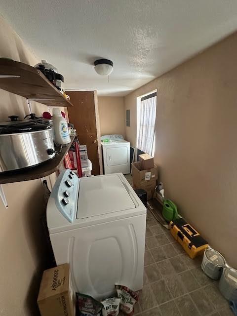 clothes washing area with washing machine and clothes dryer, dark tile patterned floors, electric panel, laundry area, and a textured ceiling