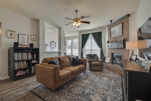 living room with visible vents, a brick fireplace, baseboards, wood finished floors, and a ceiling fan