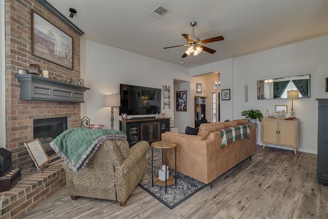 living area with visible vents, a ceiling fan, light wood finished floors, baseboards, and a brick fireplace