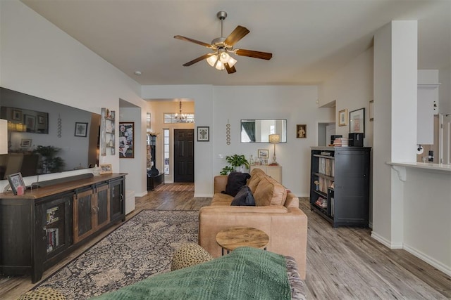 living area featuring ceiling fan with notable chandelier, light wood-type flooring, and baseboards