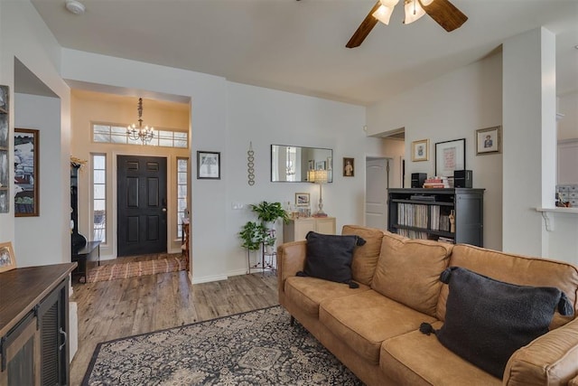 living area featuring light wood finished floors, ceiling fan with notable chandelier, and baseboards