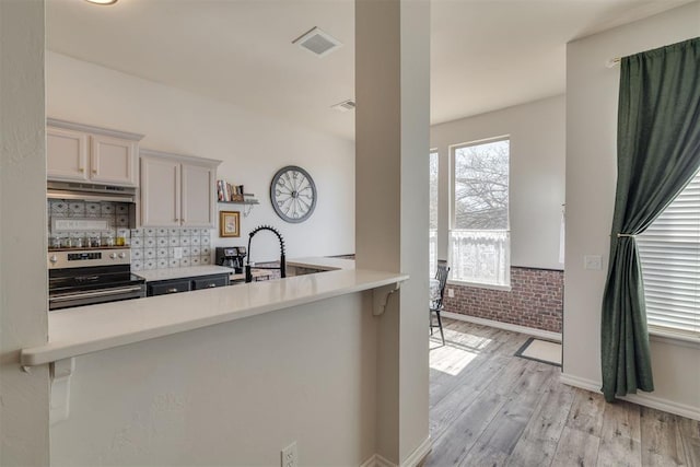 kitchen with visible vents, light wood-style flooring, under cabinet range hood, stainless steel range with electric cooktop, and brick wall