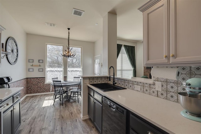 kitchen with visible vents, a sink, black dishwasher, light wood finished floors, and light countertops