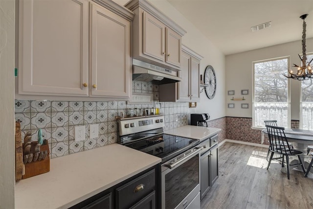 kitchen featuring visible vents, under cabinet range hood, light countertops, stainless steel electric range, and an inviting chandelier