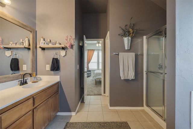 ensuite bathroom featuring tile patterned floors, a shower stall, baseboards, ceiling fan, and vanity