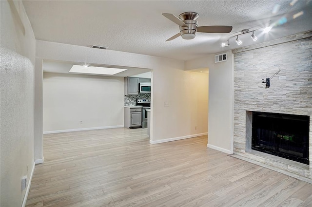 unfurnished living room featuring visible vents, light wood-style floors, a ceiling fan, and a textured ceiling