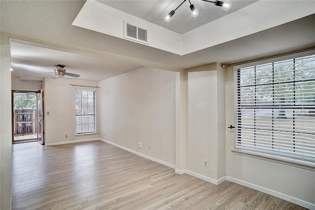 empty room with a ceiling fan, baseboards, wood finished floors, visible vents, and a textured ceiling