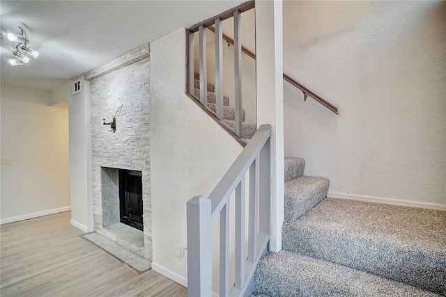 stairs with a stone fireplace, visible vents, wood finished floors, and baseboards