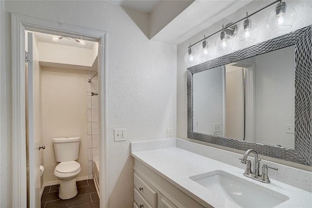 full bathroom featuring toilet, vanity, and a textured wall