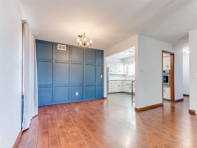 unfurnished dining area featuring visible vents, baseboards, a chandelier, wood finished floors, and a sink