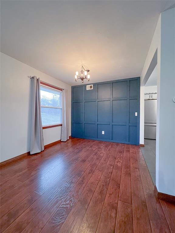 unfurnished room with dark wood finished floors, baseboards, visible vents, and a chandelier