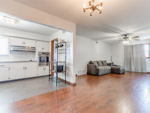 living area with visible vents, light wood-style flooring, ceiling fan with notable chandelier, and baseboards