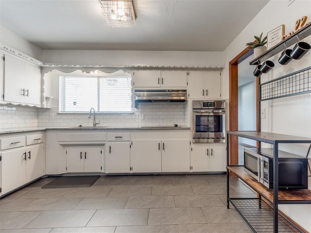 kitchen with under cabinet range hood, decorative backsplash, appliances with stainless steel finishes, and a sink