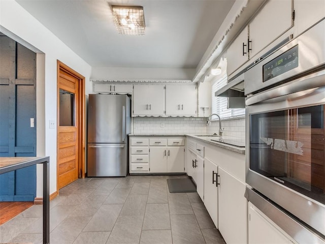 kitchen featuring a sink, tasteful backsplash, white cabinetry, stainless steel appliances, and light tile patterned floors