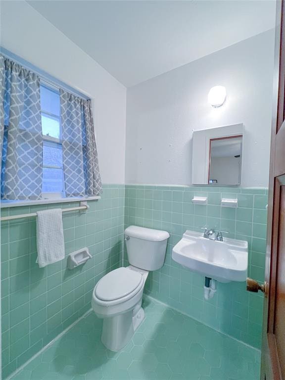 bathroom featuring tile patterned flooring, toilet, wainscoting, tile walls, and a sink