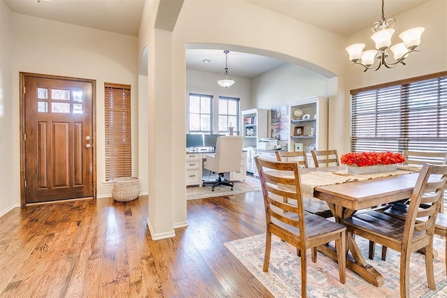 dining space with arched walkways, a chandelier, light wood-style flooring, and baseboards