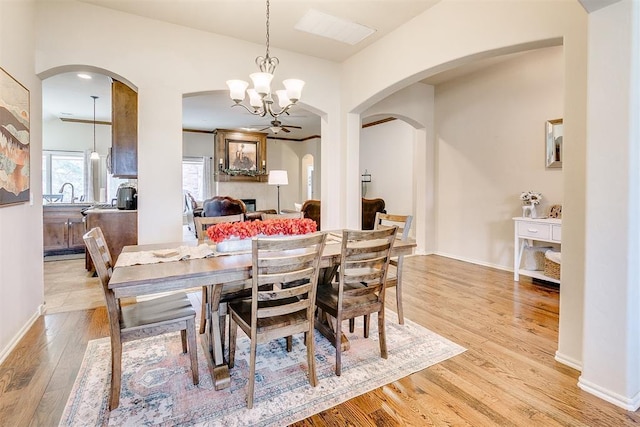 dining area with baseboards, arched walkways, light wood-type flooring, and a chandelier