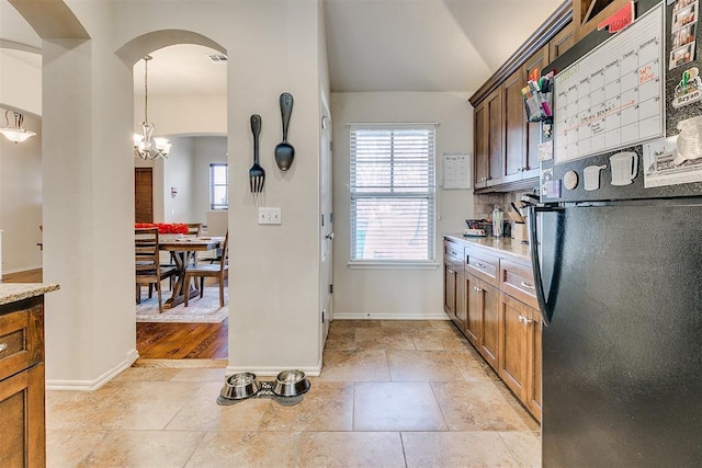 kitchen featuring baseboards, light countertops, stone tile flooring, freestanding refrigerator, and arched walkways